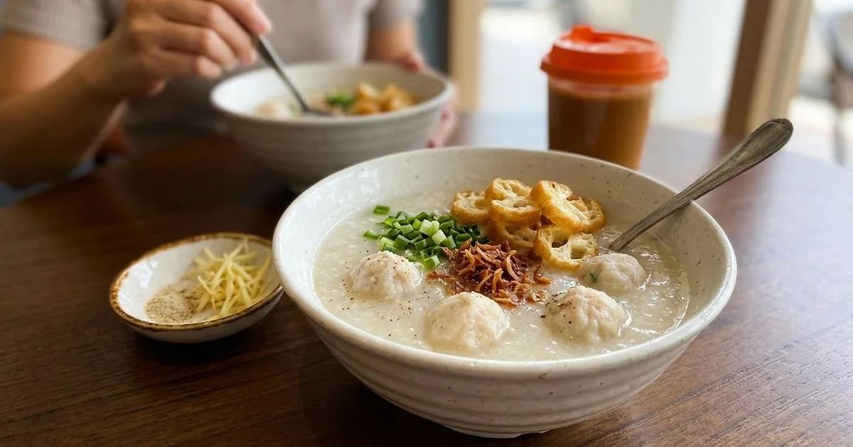 Bowl of silky porridge topped with handmade fish balls garnished with spring onions and crispy cakoi pieces