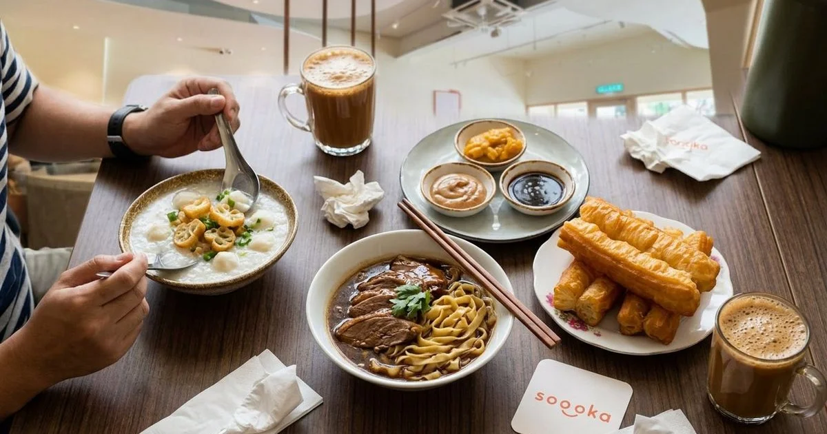 Modern cafe table set with assorted Malaysian comfort food dishes including noodles, porridge, and cakoi